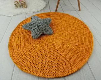 May include: A round, crocheted rug in a bright orange color with a gray crocheted star on top. The rug is made of thick yarn and has a textured surface.