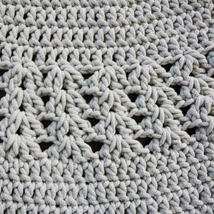 May include: Close-up of a grey crocheted rug with a textured, woven pattern. The rug is circular and made with thick yarn.