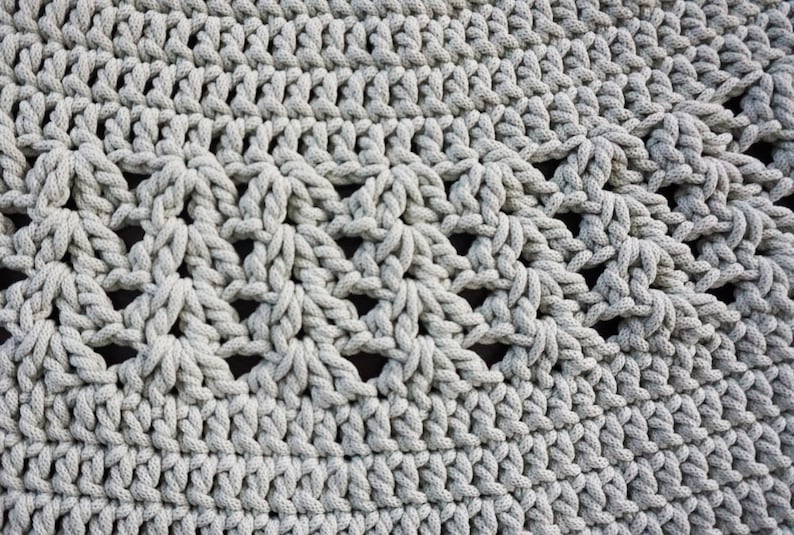 May include: Close-up of a grey crocheted rug with a textured, woven pattern. The rug is circular and made with thick yarn.