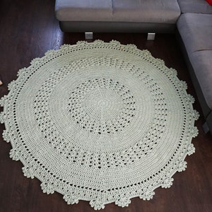 May include: A large, round, crocheted rug in a light green colour. The rug has a delicate, lacy pattern and a fringed edge.