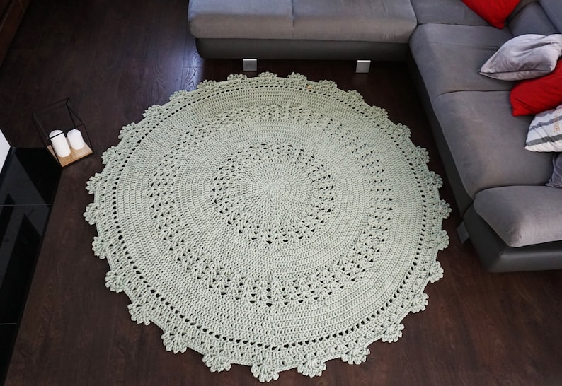 May include: A large, round, crocheted rug in a light green colour. The rug has a delicate, lacy pattern and a fringed edge.