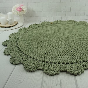 May include: A round, green crocheted rug with a delicate lace border. The rug is made of thick yarn and has a soft, textured surface.