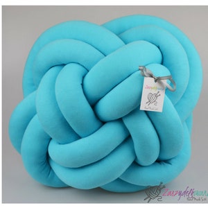 Könnte beinhalten: Ein hellblaues, geknotetes Kissen mit einem kleinen Etikett, auf dem "Zaszylekwanka Hand Made Stuff" steht.