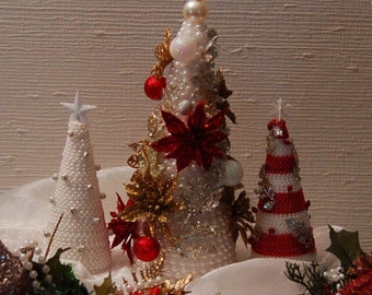 May include: Three white Christmas trees decorated with red and gold ornaments, white beads, and a red poinsettia. The trees are arranged on a white sheer fabric with white pearl beads.