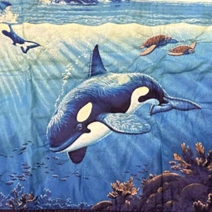 May include: A blue and white quilted throw pillow with a colorful image of orcas swimming in the ocean. The pillow features a dark blue border with a decorative pattern.