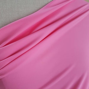Può includere: Un primo piano di un tessuto rosa brillante, che mostra la sua trama e il suo drappeggio. Il tessuto è liscio e setoso, con un leggero luccichio. Il testo "pink candy" è visibile nella parte inferiore dell'immagine.