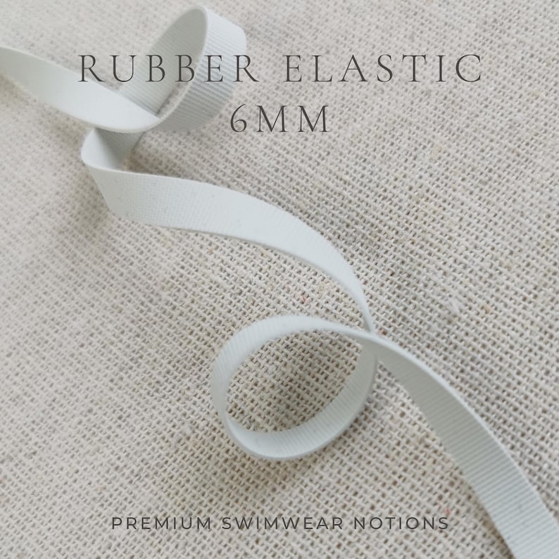 May include: A white rubber elastic band measuring 6mm in width, featuring a ribbed texture throughout its length. The elastic is coiled in a loose loop. The text RUBBER ELASTIC 6MM and PREMIUM SWIMWEAR NOTIONS is printed on the image.