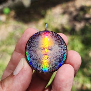 Peut inclure: Un pendentif rond avec un motif de visage de soleil. Le pendentif présente un effet irisé arc-en-ciel sur les bords et un centre jaune et orange. Il est maintenu par une bélière argentée.