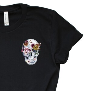 May include: Black t-shirt with a white skull design. The skull's eye sockets are filled with pink, yellow, and burgundy flowers.