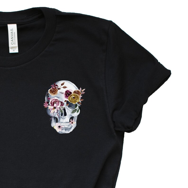 May include: Black t-shirt with a white skull design. The skull's eye sockets are filled with pink, yellow, and burgundy flowers.