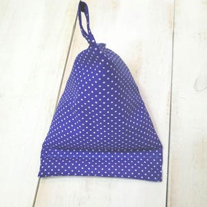 May include: A blue fabric bag with white polka dots, featuring a loop at the top. The bag is triangular in shape and appears to be made of a soft material. The background is a light-colored wooden surface.