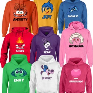 May include: A collection of hooded sweatshirts in various colors, each featuring a character face and emotion label. Colors include orange (Anxiety), yellow (Joy), blue (Sadness), red (Anger), purple (Fear), pink (Nostalgia), green (Envy), white (Bloofy), and magenta (Embarrassment).
