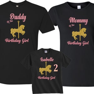 May include: Three black t-shirts with pink and gold glitter text and a gold glitter carousel horse design. The shirts say "Daddy of the Birthday Girl", "Mommy of the Birthday Girl", and "Isabelle 2 Birthday Girl".