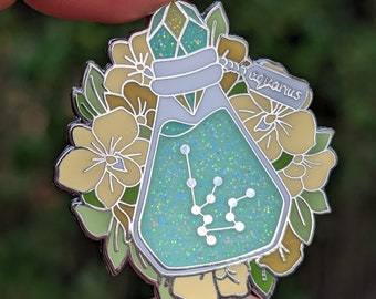May include: A silver enamel pin featuring a glass bottle filled with green glitter and the constellation Aquarius. The bottle is topped with a crystal and surrounded by yellow flowers.