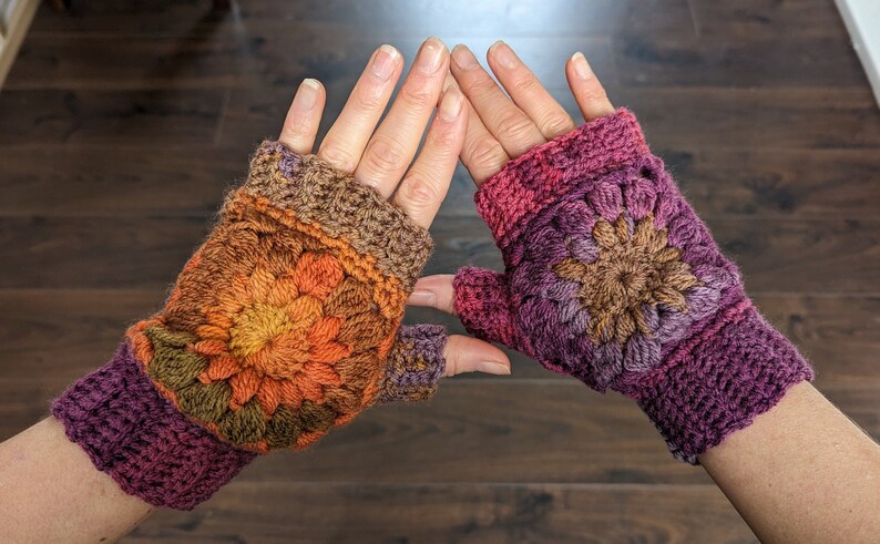 Peut inclure: Une paire de mitaines en crochet avec un motif floral color&eacute;. Les mitaines sont faites avec une vari&eacute;t&eacute; de nuances de marron, orange, violet et rose.