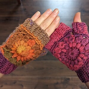 Peut inclure: Une paire de mitaines en crochet dans des tons de brun, orange, rose et violet. Les mitaines pr&eacute;sentent un motif floral et un trou pour le pouce.