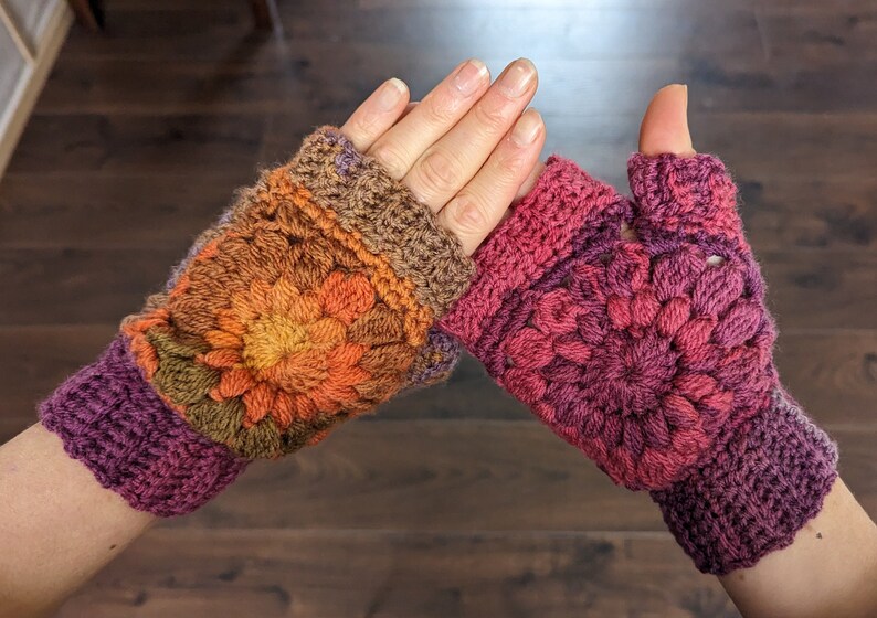 Peut inclure: Une paire de mitaines en crochet dans des tons de brun, orange, rose et violet. Les mitaines pr&eacute;sentent un motif floral et un trou pour le pouce.