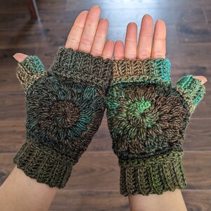 Peut inclure: Une paire de mitaines sans doigts de couleur marron, verte et bleue. Les mitaines pr&eacute;sentent un motif circulaire avec un tricot textur&eacute;.