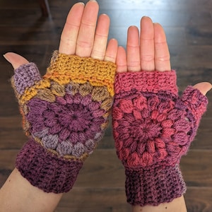 Peut inclure: Une paire de mitaines en crochet avec un motif de granny squares color&eacute;. Les mitaines sont faites avec un m&eacute;lange de fils rose, violet, orange et marron.