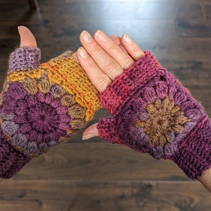 Peut inclure: Une paire de mitaines en crochet avec un motif floral color&eacute; dans les tons de violet, marron, orange et rose.