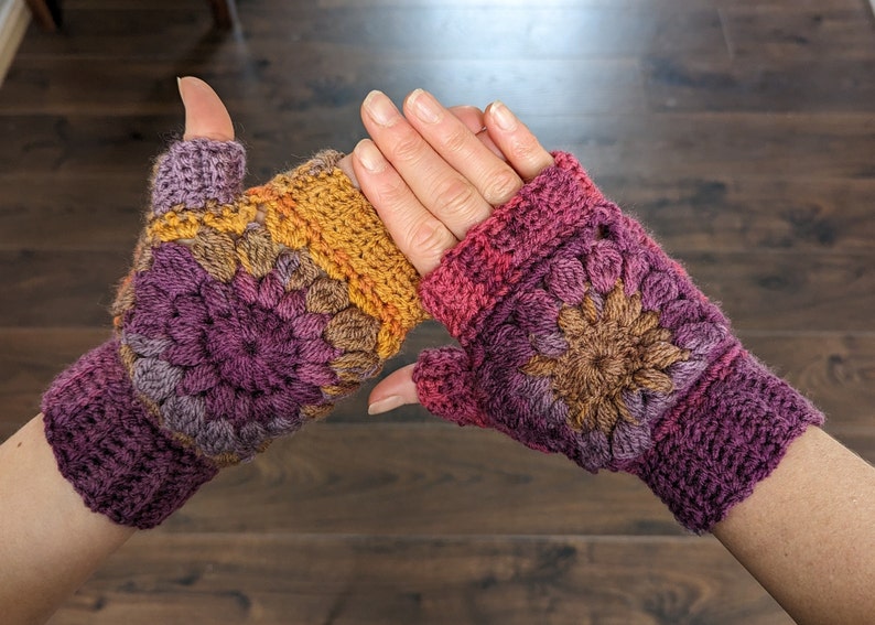 Peut inclure: Une paire de mitaines en crochet avec un motif floral color&eacute; dans les tons de violet, marron, orange et rose.