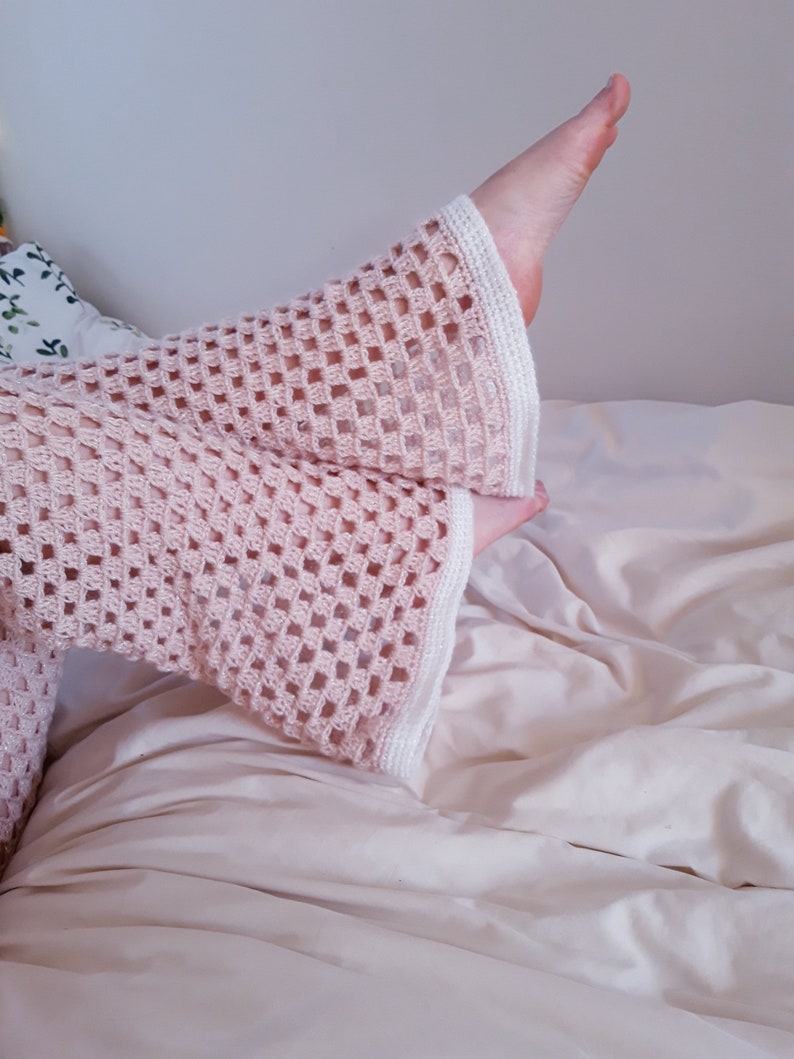 May include: Pale pink crochet sleeves with a square openwork design and white edging. The sleeves are on a bed with a cream-coloured duvet. The image has a soft, delicate feel.