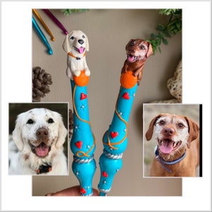 May include: Two handmade crochet hooks with dog toppers. One hook has a white dog with brown spots and a red heart on its chest. The other hook has a brown dog with a red heart on its chest. Both hooks are blue with orange and white accents.
