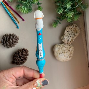 May include: A blue and white crochet hook with a white dog figurine on top. The hook has a label that says "Mr. Dash".