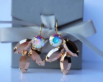 May include: Rose gold earrings with iridescent crystal accents. The earrings feature a cluster of five rose gold leaves with a large iridescent crystal in the center.