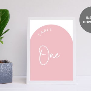 May include: Printable table number sign with a pink background and white text. The text reads "Table One" in a modern script font.
