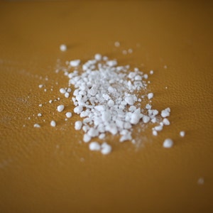 Pode incluir: Grânulos brancos espalhados sobre uma superfície marrom.