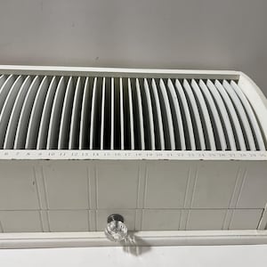 May include: A white wooden desk organizer with a curved top and multiple vertical dividers. The front of the organizer has a series of numbers from 2 to 31. A small drawer with a glass knob is visible.