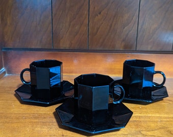 May include: Three black octagonal ceramic coffee cups and saucers. The cups and saucers are all the same size and shape.