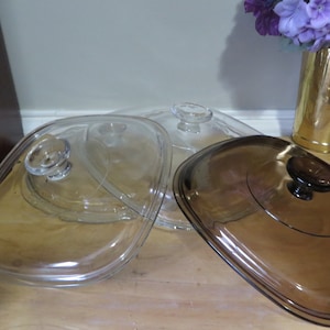 May include: Three glass lids for a casserole dish. Two are clear glass and one is brown glass. All three lids have a knob on top.