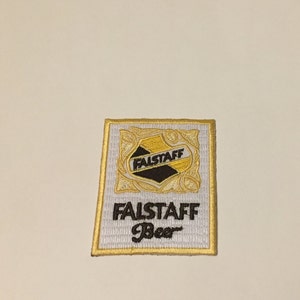 May include: A white embroidered patch with a gold border. The patch features a black and gold crest with the word "Falstaff" and the text "Falstaff Beer" in black.