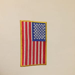 May include: A small embroidered American flag patch with a yellow border. The flag is red, white, and blue.