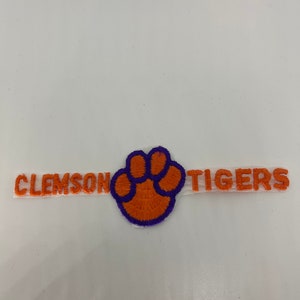 May include: Orange and purple embroidered patch with the words "Clemson Tigers" and a paw print.