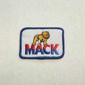 Pode incluir: Um remendo bordado azul e branco com um bulldog amarelo e a palavra "MACK" em letras vermelhas e azuis.