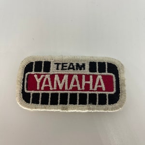Op de afbeelding: Witte geborduurde patch met zwarte en rode accenten. De patch heeft de tekst "TEAM YAMAHA" in witte letters.