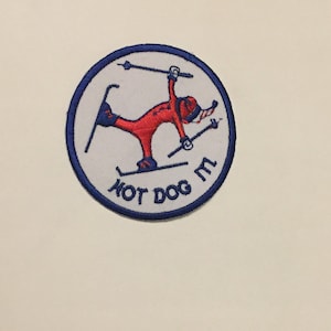 May include: A white and blue circular patch with a red stick figure skiing. The text "HOT DOG" is written in blue below the figure.