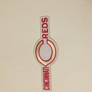 Puede incluir: Un parche bordado blanco y rojo con las palabras "Cincinnati Reds" y una "C" roja con un contorno blanco.