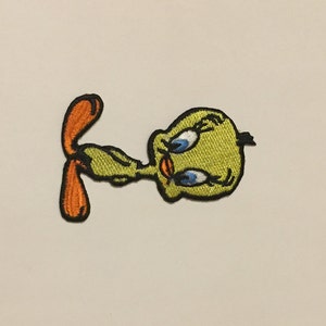 May include: A yellow embroidered iron-on patch of Tweety Bird from Looney Tunes. Tweety Bird is looking to the left with his eyes closed and his mouth open. He has a black beak and black eyebrows. His feet are orange.