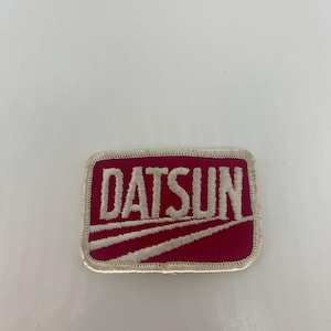 May include: A red embroidered patch with white stitching that reads "DATSUN".