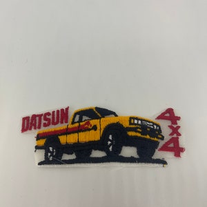May include: Yellow embroidered patch of a Datsun pickup truck with a red stripe and the text "Datsun" and "4x4".
