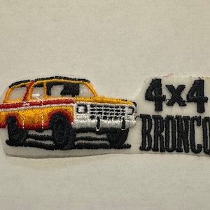 May include: An embroidered patch featuring a yellow and red Ford Bronco with the text "4x4 Bronco" in black.