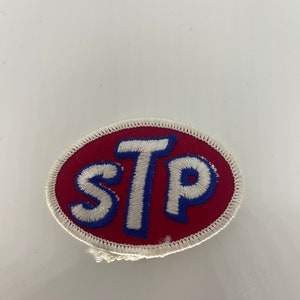 May include: A red oval-shaped patch with white stitching around the edges. The letters "STP" are embroidered in white with blue outlines.