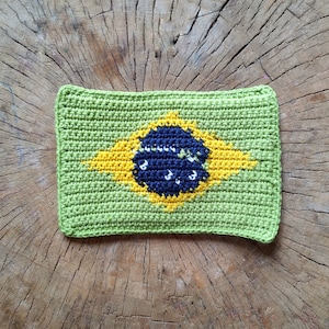 May include: A green crocheted square with a yellow star and a blue circle in the center, representing the Brazilian flag.