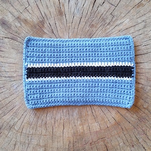 May include: A blue crocheted rectangle with a black and white stripe in the center. The rectangle is made of yarn and has a textured surface.