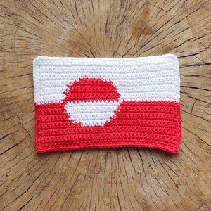 May include: A crocheted flag of Greenland, featuring a red and white circle on a white background with a red bottom half.
