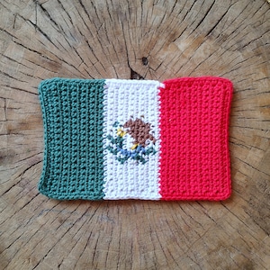 Könnte beinhalten: Gehäkelte mexikanische Flagge mit grünen, weißen und roten Streifen und einem Wappen in der Mitte.